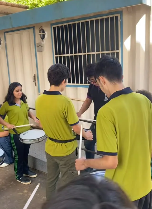 Alumnos con uniforme verde ensayando con tambores de la banda lisa