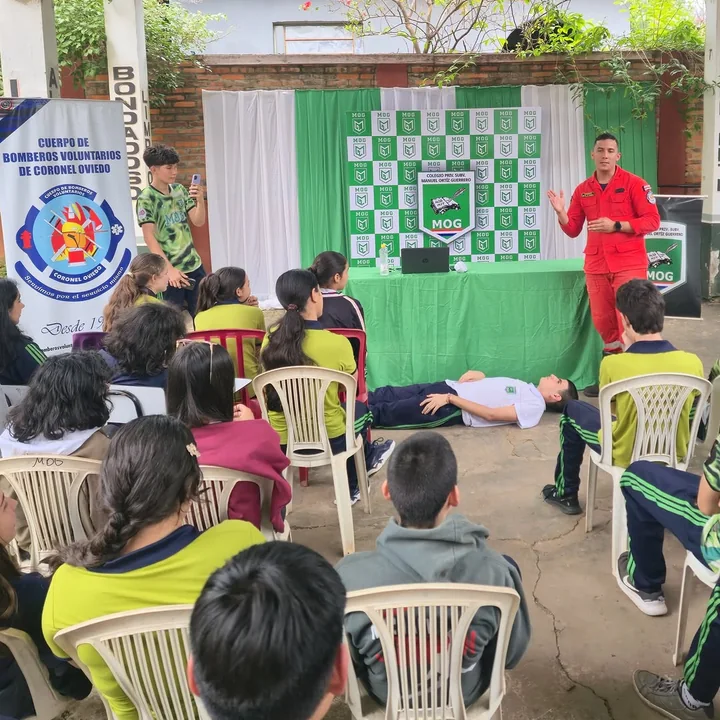 Alumnos sentados en el patio escuchan una charla de primeros auxilios de los Bomberos Voluntarios de Coronel Oviedo